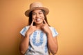 Young beautiful asian girl wearing casual t-shirt and hat standing over yellow background Smiling with open mouth, fingers Royalty Free Stock Photo