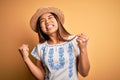 Young beautiful asian girl wearing casual t-shirt and hat standing over yellow background very happy and excited doing winner Royalty Free Stock Photo