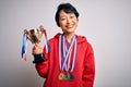 Young beautiful asian girl winner holding trophy wearing medals over white background with a happy face standing and smiling with Royalty Free Stock Photo