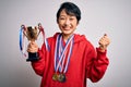 Young beautiful asian girl winner holding trophy wearing medals over white background screaming proud and celebrating victory and Royalty Free Stock Photo