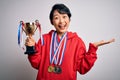 Young beautiful asian girl winner holding trophy wearing medals over white background very happy and excited, winner expression Royalty Free Stock Photo