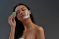 Young beautiful asian half naked woman with closed eyes using cleaning face with facial sponge while posing against dark Royalty Free Stock Photo