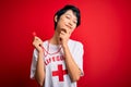 Young beautiful asian lifeguard girl wearing t-shirt with red cross using whistle looking confident at the camera smiling with