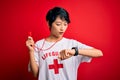 Young beautiful asian lifeguard girl wearing t-shirt with red cross using whistle Looking at the watch time worried, afraid of