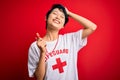 Young beautiful asian lifeguard girl wearing t-shirt with red cross using whistle smiling confident touching hair with hand up
