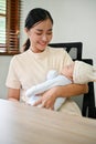 Young beautiful Asian mother working at home and holding her baby in her arms Royalty Free Stock Photo