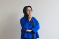 Young beautiful Asian Muslim woman, wearing glasses and blue blazer thinking while propping up chin Royalty Free Stock Photo