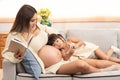 Young beautiful Asian pregnant women reading the book and her toddler daughter laying down having ear on mother tummy. Little girl Royalty Free Stock Photo