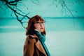 A young Asian redhead woman wearing a warm coat standing in a winter park by the coast. A cold winter walk outdoors, emphasizing