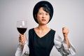 Young beautiful asian sommelier girl drinking glass of red wine over isolated white background annoyed and frustrated shouting