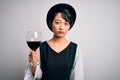 Young beautiful asian sommelier girl drinking glass of red wine over isolated white background with a confident expression on