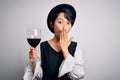 Young beautiful asian sommelier girl drinking glass of red wine over isolated white background cover mouth with hand shocked with