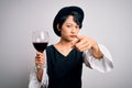 Young beautiful asian sommelier girl drinking glass of red wine over isolated white background pointing with finger to the camera Royalty Free Stock Photo