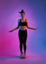 Young Beautiful Asian sports girl doing exercises with jumping rope in fitness studio neon background. Woman exercising with Royalty Free Stock Photo