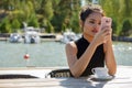 Young beautiful Asian tourist woman using phone at restaurant by the pier Royalty Free Stock Photo