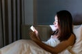 Young beautiful Asian woman in bed using mobile phone late at night in dark bedroom. Smartphone, internet addiction, Insomnia Royalty Free Stock Photo