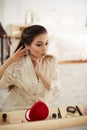 A young beautiful Asian woman in a beige lace dressing gown put on morning makeup and wears earrings . shallow depth of focus. Royalty Free Stock Photo