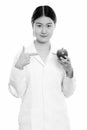 Young beautiful Asian woman doctor holding and pointing at red apple while looking at camera Royalty Free Stock Photo