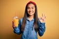 Young beautiful asian woman drinking healthy glass of orange juice over yellow background doing ok sign with fingers, excellent Royalty Free Stock Photo
