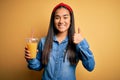 Young beautiful asian woman drinking healthy glass of orange juice over yellow background happy with big smile doing ok sign, Royalty Free Stock Photo