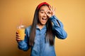 Young beautiful asian woman drinking healthy glass of orange juice over yellow background with happy face smiling doing ok sign Royalty Free Stock Photo