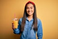 Young beautiful asian woman drinking healthy glass of orange juice over yellow background with a happy face standing and smiling Royalty Free Stock Photo