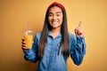 Young beautiful asian woman drinking healthy glass of orange juice over yellow background surprised with an idea or question Royalty Free Stock Photo