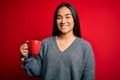 Young beautiful asian woman drinking mug of coffee standing over isolated red background with a happy face standing and smiling Royalty Free Stock Photo