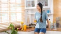 Young beautiful asian woman drinking orange juice and smiling while standing by window in kitchen background, peolpe and healthy