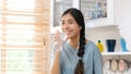 Young beautiful asian woman drinking water wearning earphones and standing by window in kitchen background, peolpe and healthy