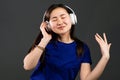 Young beautiful asian woman with headphones in modern wear enjoying and dancing on grey background. Radio, melody