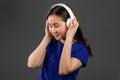 Young beautiful asian woman with headphones in modern wear enjoying and dancing on grey background. Radio, melody
