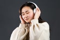 Young beautiful asian woman with headphones in modern wear enjoying and dancing on grey background. Radio, melody