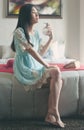 Young beautiful asian woman holding bottle of perfume and applying on her neck in a room Royalty Free Stock Photo