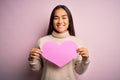 Young beautiful asian woman holding pink heart standing over isolated background with a happy face standing and smiling with a Royalty Free Stock Photo