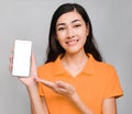 Young beautiful asian woman,long black hair, wore orange t shirt,smile and raise the mobile phone screen blank on gray background Royalty Free Stock Photo