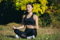 Young beautiful asian woman performs fitness yoga exercises, sitting in lotus position on the grass and meditating in the park Royalty Free Stock Photo