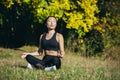 Young beautiful asian woman performs fitness yoga exercises, sitting in lotus position on the grass and meditating in the park Royalty Free Stock Photo