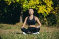 Young beautiful asian woman performs fitness yoga exercises, sitting in lotus position on the grass and meditating in the park Royalty Free Stock Photo