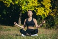 Young beautiful asian woman performs fitness yoga exercises, sitting in lotus position on the grass and meditating in the park Royalty Free Stock Photo