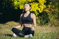 Young beautiful asian woman performs fitness yoga exercises, sitting in lotus position on the grass and meditating in the park Royalty Free Stock Photo