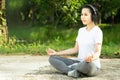 Young beautiful asian woman practices yoga and meditates outdoor sitting in lotus pose in the park and listening to music on Royalty Free Stock Photo