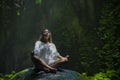 Young beautiful Asian woman practicing Yoga posing sitting in lotus position meditating over a stone in a stunning natural landsca Royalty Free Stock Photo