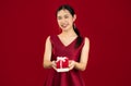 Young beautiful asian woman in red luxury dress holding and giving present red box white bow pose looking and smiling Royalty Free Stock Photo