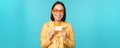 Young beautiful asian woman showing credit card, smiling, choosing bank, standing over blue background