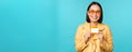 Young beautiful asian woman showing credit card, smiling, choosing bank, standing over blue background