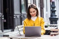 Young beautiful Asian woman sitting in coffee shop at wooden table, drinking coffee and using laptop. Girl browsing internet, Royalty Free Stock Photo