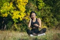 Young beautiful Asian woman sitting in lotus position in the park, relaxing after fitness and running, listening to music on Royalty Free Stock Photo