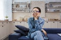 Young beautiful asian woman thinking in glasses sitting on sofa at home in living room Royalty Free Stock Photo