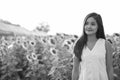 Young beautiful Asian woman thinking while looking up in the field of blooming sunflowers Royalty Free Stock Photo